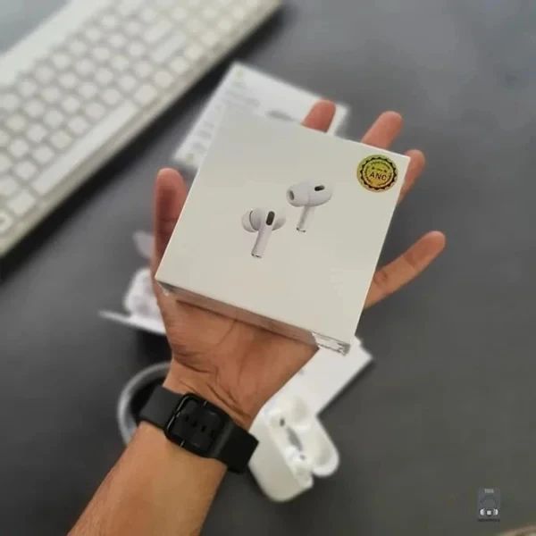 Hand holding a white box with earbud illustrations on a desk with a keyboard in the background